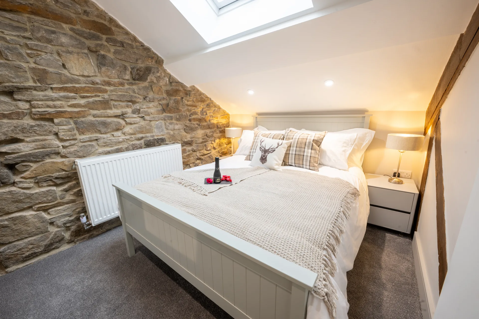 White bed beneath a skylight beside an exposed stone wall