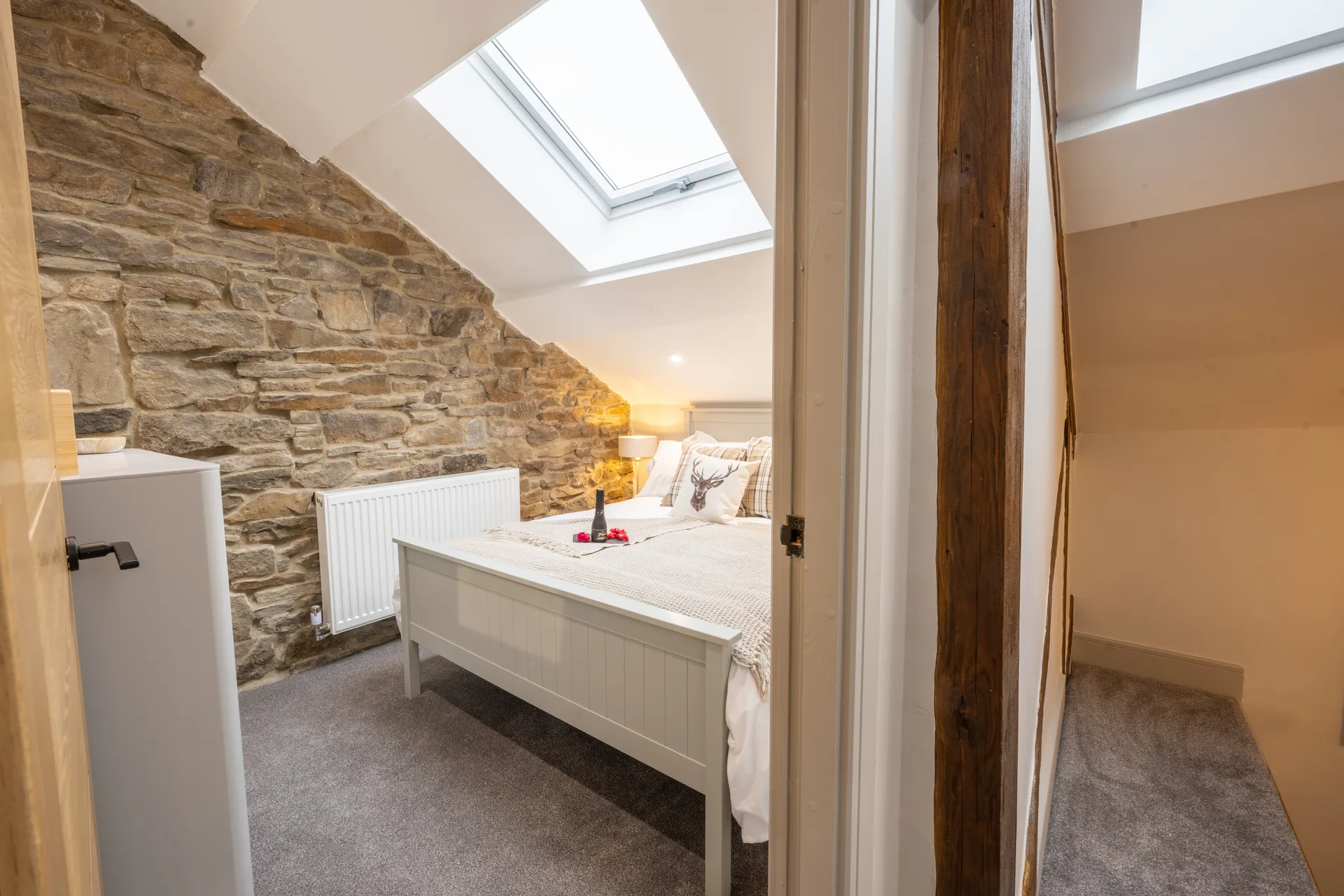 Bedroom with a white bed, exposed stone wall and skylight