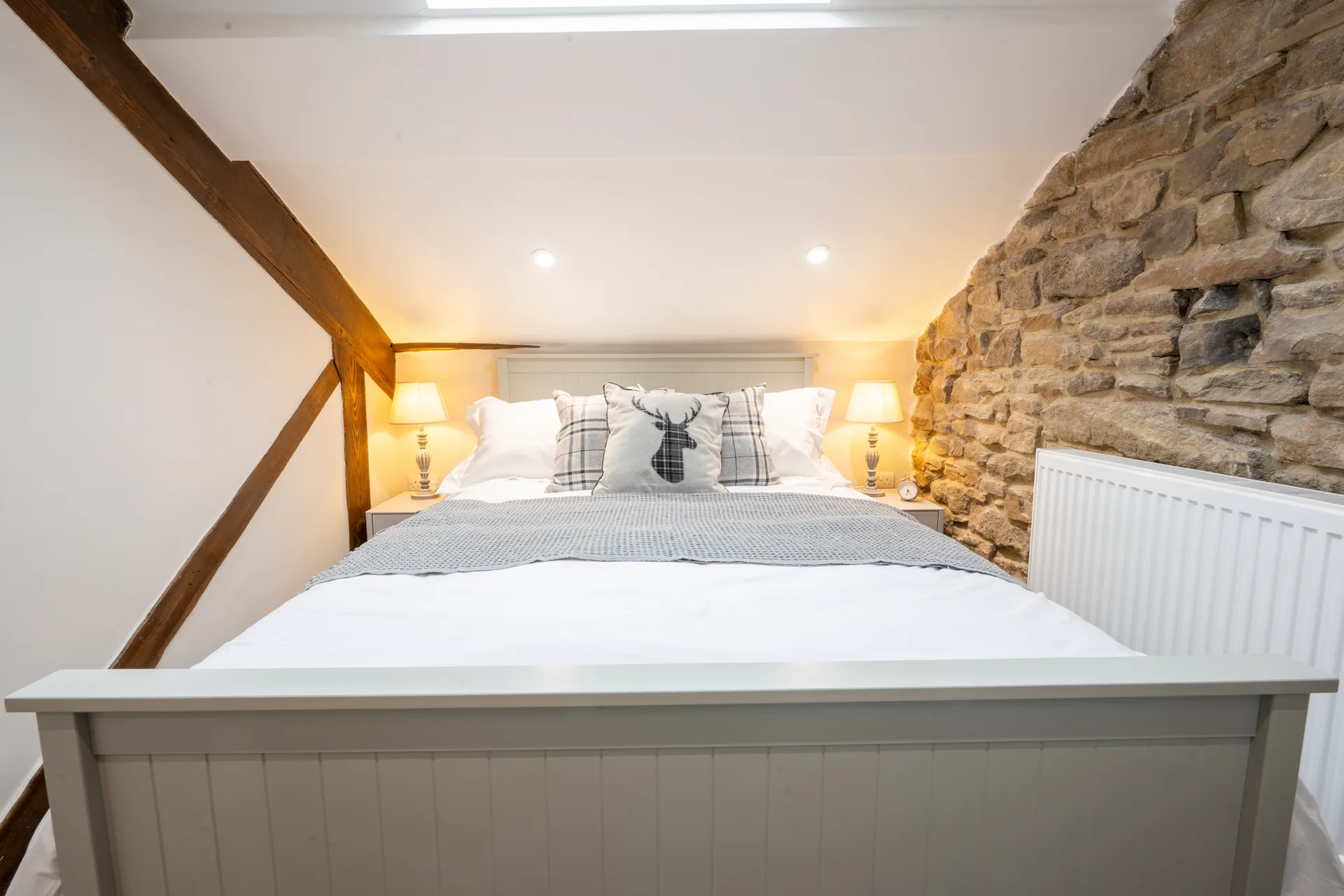 White bed beneath wooden beams beside an exposed stone wall